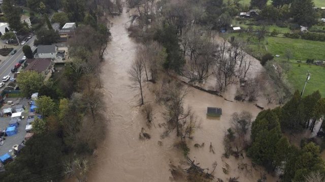 Banjir Sungai San Lorenzo yang dilanda badai membanjiri sepanjang Ocean Street Extension di Santa Cruz, California, di sebelah kanan, Senin (9/1/2023) (Foto: AP)