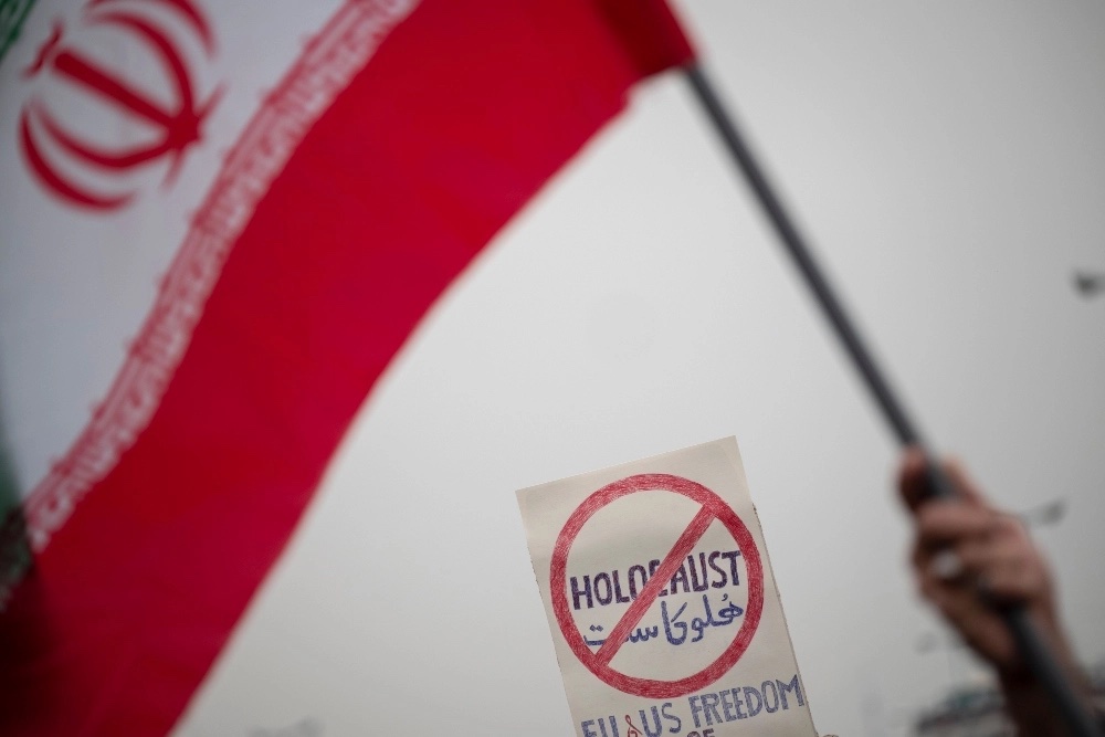 Seorang jamaah mengibarkan bendera Iran di depan plakat anti-Holocaust saat menghadiri protes atas pembakaran Al-Qu'ran setelah upacara Salat Jumat Teheran di masjid Agung Imam Khomeini, 27 Januari 2023. (Foto oleh Morteza Nikoubaz)